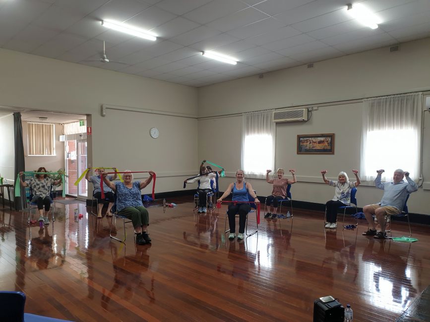Mulher idosa realizando exercício de fortalecimento com cadeira em ambiente doméstico seguro