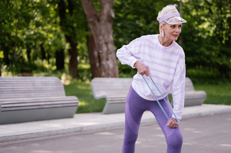 Mulher idosa realizando exercício de fortalecimento de pernas com faixa elástica