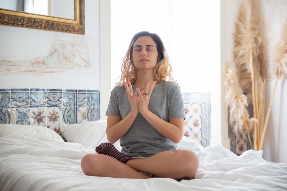Mulher meditando em quarto iluminado naturalmente, expressão tranquila